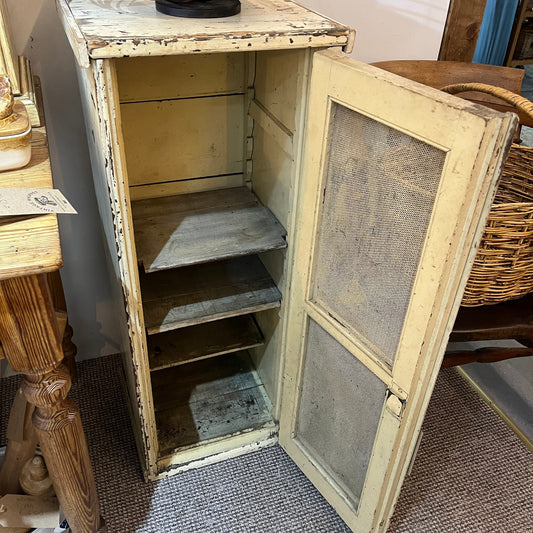 A distressed vintage wooden cabinet with a cream-colored frame and open door, showing three interior shelves, photographed in a home setting.