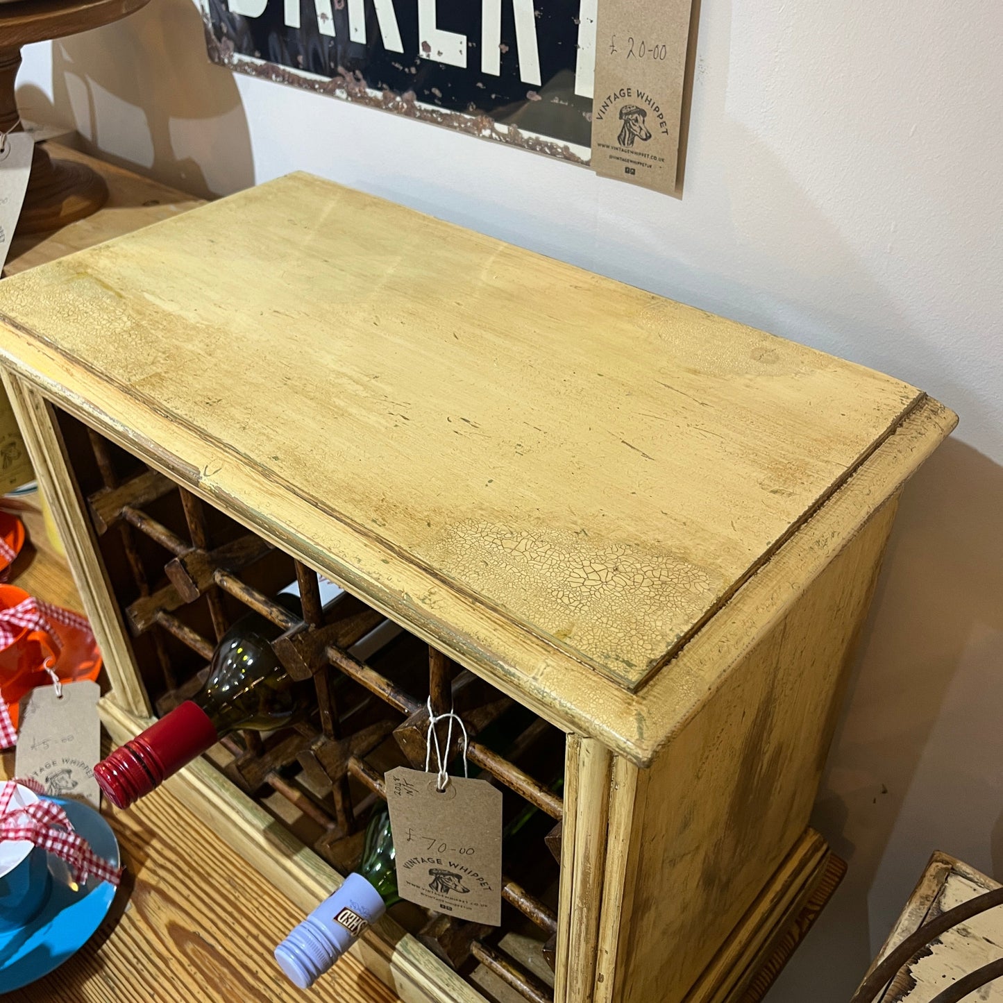 A rustic, distressed light yellow wooden wine rack cabinet with a herringbone pattern, shown in a home setting with wine bottles stored inside.