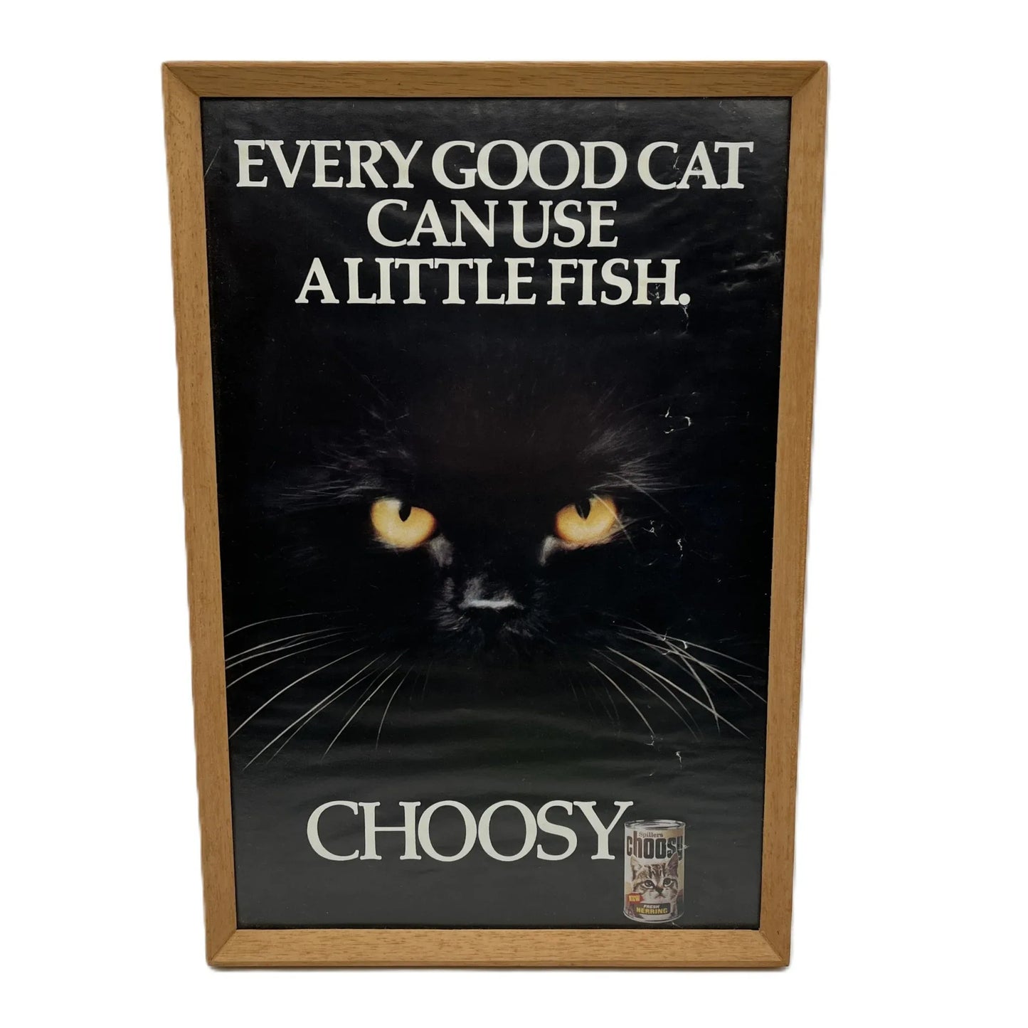 This is a vintage framed advertising poster for Choosy Cat Food. From the early 1980s, this one reads "every good cat can use a little fish". It has been framed in a wooden frame sometime in the past, which has helped to preserve it.