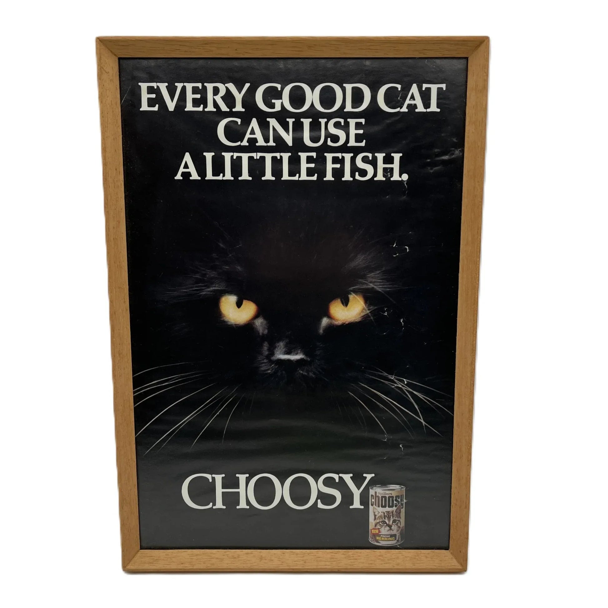 This is a vintage framed advertising poster for Choosy Cat Food. From the early 1980s, this one reads "every good cat can use a little fish". It has been framed in a wooden frame sometime in the past, which has helped to preserve it.