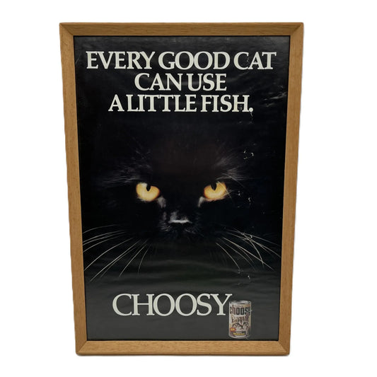 This is a vintage framed advertising poster for Choosy Cat Food. From the early 1980s, this one reads "every good cat can use a little fish". It has been framed in a wooden frame sometime in the past, which has helped to preserve it.