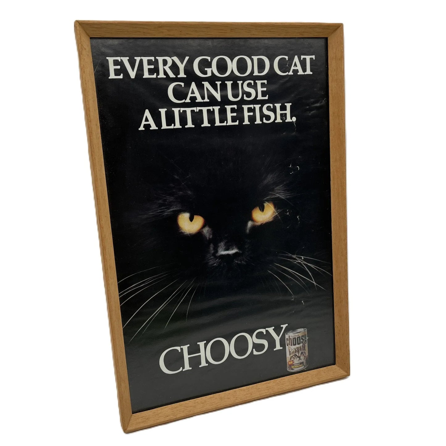 This is a vintage framed advertising poster for Choosy Cat Food. From the early 1980s, this one reads "every good cat can use a little fish". It has been framed in a wooden frame sometime in the past, which has helped to preserve it.