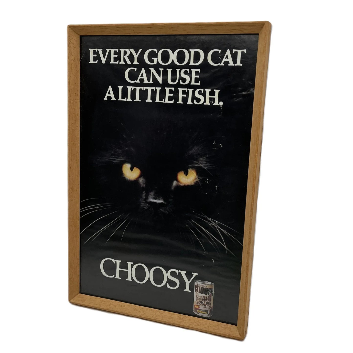 This is a vintage framed advertising poster for Choosy Cat Food. From the early 1980s, this one reads "every good cat can use a little fish". It has been framed in a wooden frame sometime in the past, which has helped to preserve it.