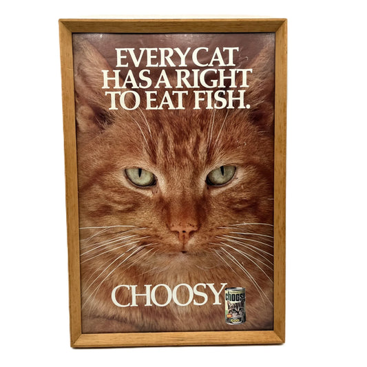 This is a vintage framed advertising poster for Choosy Cat Food. From the early 1980s, this one reads "every cat has the right to eat fish". It has been framed in a wooden frame sometime in the past, which has helped to preserve it.