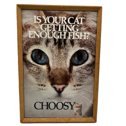 This is a vintage framed advertising poster for Choosy Cat Food. From the early 1980s, this one reads "is your cat getting enough fish". It has been framed in a wooden frame sometime in the past, which has helped to preserve it.