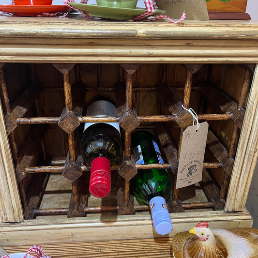 A rustic wooden wine rack with a grid design holding two wine bottles, one with a red foil and one with a blue cap, set against a light wood cabinet background.