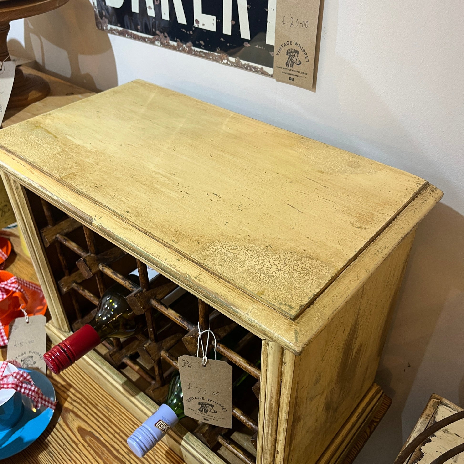 A rustic, distressed light yellow wooden wine rack cabinet with a herringbone pattern, shown in a home setting with wine bottles stored inside.