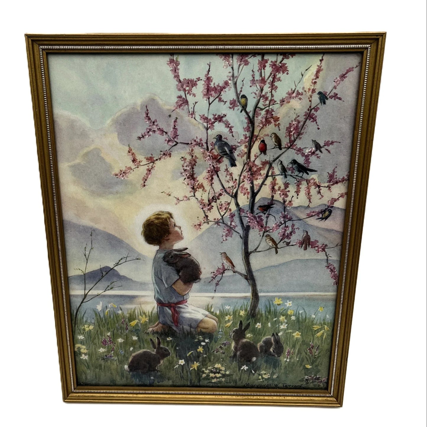 This is a framed print of the painting "Morning Carol" by the British illustrator Margaret Tarrant (1888-1959). The artwork depicts a child holding a rabbit, surrounded by other rabbits and birds under a blossoming tree, in a pastoral setting. 