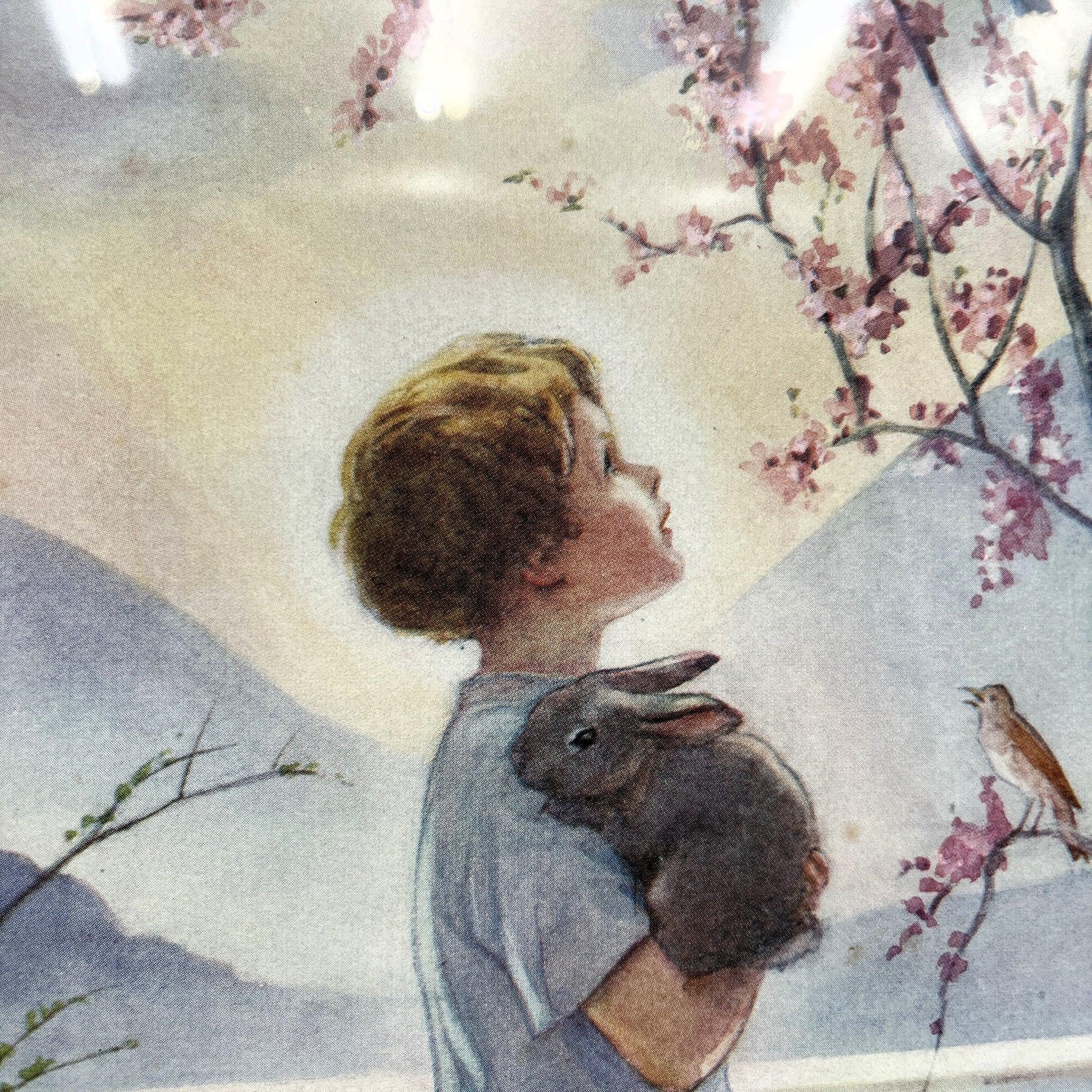 This is a framed print of the painting "Morning Carol" by the British illustrator Margaret Tarrant (1888-1959). The artwork depicts a child holding a rabbit, surrounded by other rabbits and birds under a blossoming tree, in a pastoral setting. 