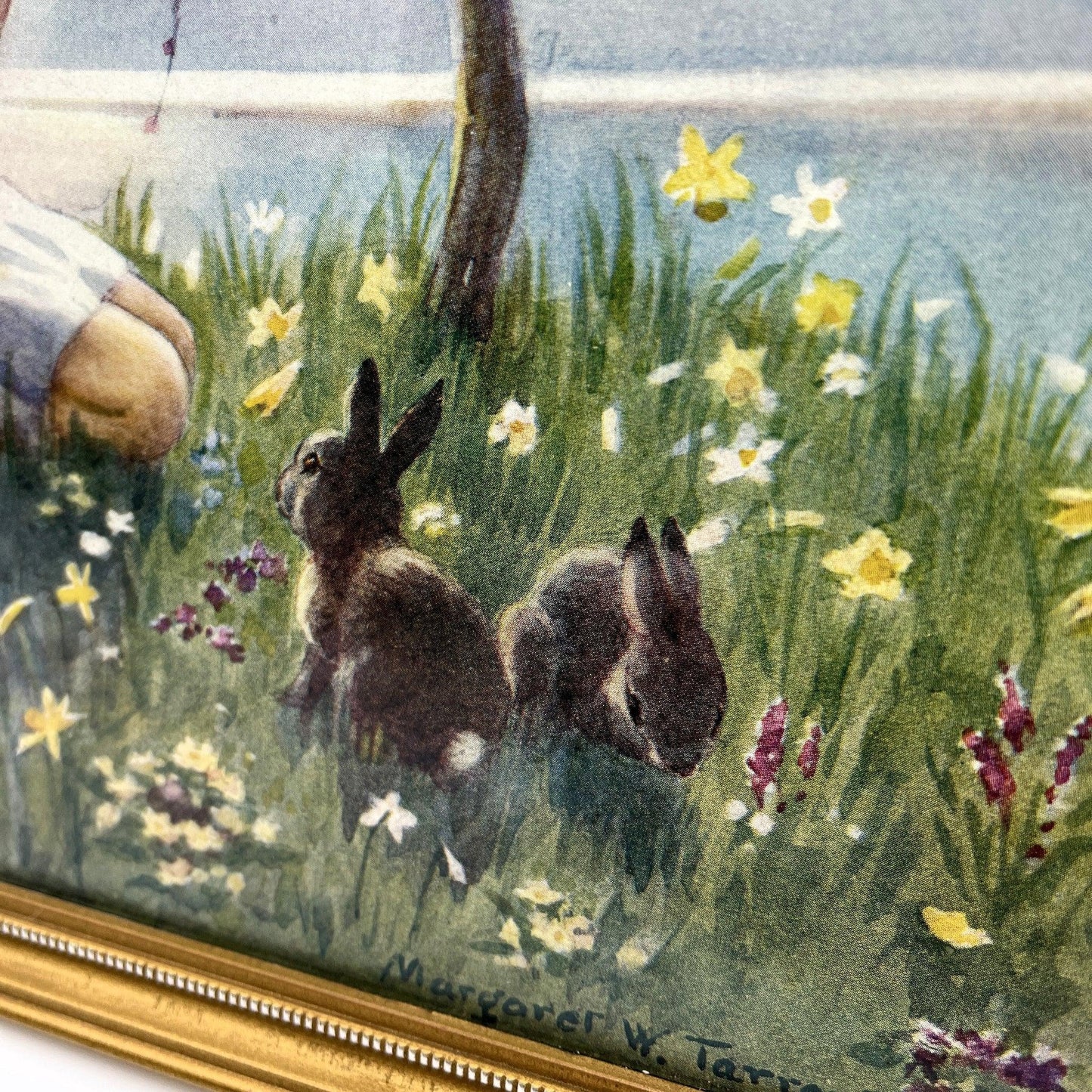 This is a framed print of the painting "Morning Carol" by the British illustrator Margaret Tarrant (1888-1959). The artwork depicts a child holding a rabbit, surrounded by other rabbits and birds under a blossoming tree, in a pastoral setting. 